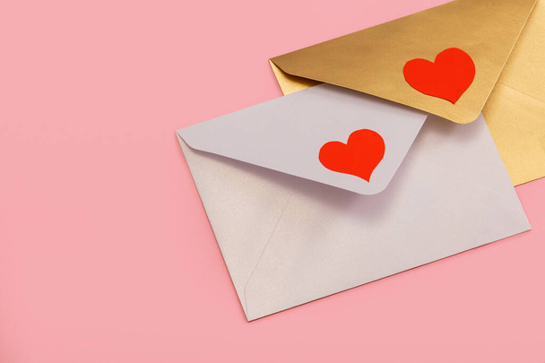 light mother-of-pearl and golden paper envelopes with red hearts isolated on pink background - Fotó, kép