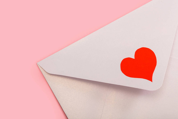 licht parelmoer papieren envelop met rood hart geïsoleerd op roze achtergrond - Foto, afbeelding