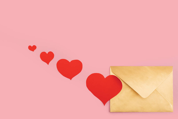 Golden paper envelope with red hearts near it isolated on pink background - Zdjęcie, obraz