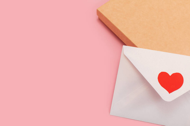 light mother-of-pearl paper envelope with red heart on the gift box isolated on pink background - Fotó, kép
