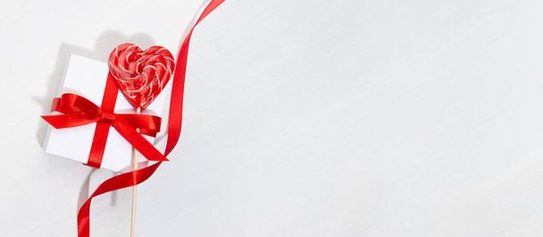 Banner festivo elegante clásico con amor - cajas de regalo blancas con lazo rojo, cinta rizada, corazones de piruletas dulces en tablero de madera blanca. - Foto, Imagen