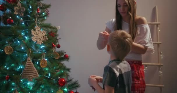 Mutter und ihr Sohn hängen Weihnachtsbaumspielzeug an den Weihnachtsbaum - Filmmaterial, Video