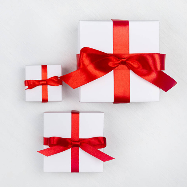 Different bright simple white gift box with red silk ribbon on white wooden table, top view, square. - Valokuva, kuva