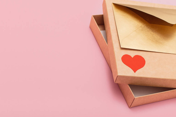 golden color paper envelope with red heart on the gift box free inside isolated on pink background - Foto, afbeelding