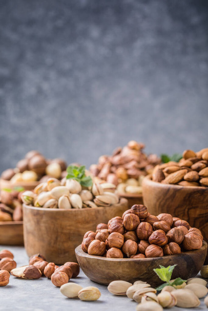 Assortiment de noix dans un bol en bois, sur un fond gris. Noisettes, pistaches, amandes, noix du Brésil, noix de cajou - Photo, image