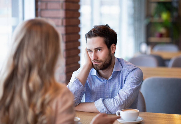 Jonge man voelt zich verveeld op saaie date in restaurant, teleurgesteld in zijn partner - Foto, afbeelding