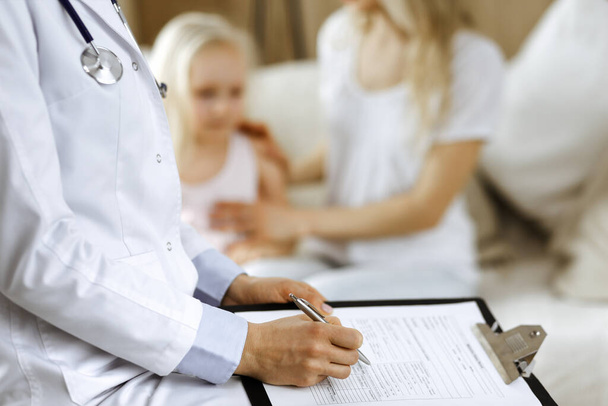 Doctor and patient. Pediatrician using clipboard while examining little girl with her mother at home. Happy cute caucasian child at medical exam. Medicine concept - Photo, image