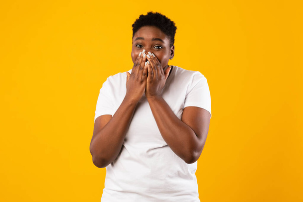 Plus-Size-afrikanische Dame, die lachend den Mund mit Händen bedeckt, gelber Hintergrund - Foto, Bild