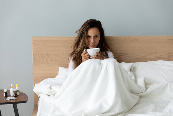 Unhappy woman feeling holding cup of tea, sitting in bed - Фото, зображення