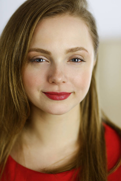 Head shot of a smart confident smiling millennial european woman standing with folded arms at home. Attractive young teenager student girl freelancer looking at camera, dressed in red - Foto, imagen