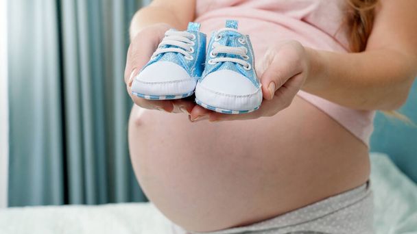 Primer plano de las pequeñas botas de bebé recién nacidas azules en las manos de yougn mujer embarazada - Foto, imagen