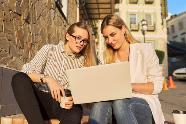 Two young smiling women looking at laptop monitor, sitting outdoors - Photo, Image