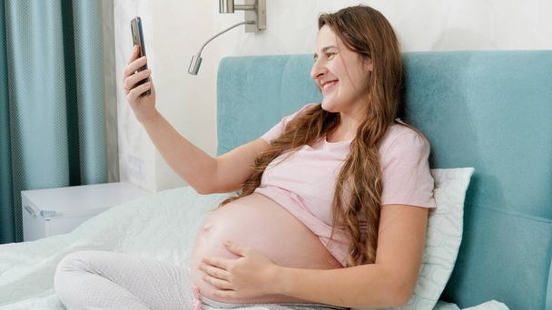 Portrait of happy smiling pregnant woman having video talk or conference on smartphone. - Foto, Imagen