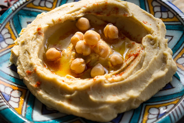 Close-up foto van verse zelfgemaakte hummus op kleurrijke keramische plaat. Evenwichtige maaltijd foto. Gezond eten concept. Authentiek voedsel uit het Midden-Oosten.  - Foto, afbeelding