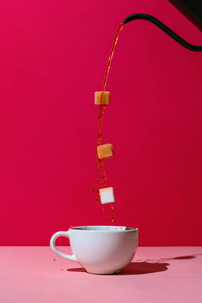 Coffee poured from black pot in a white cup with three levitating sugar cubes on red - Zdjęcie, obraz