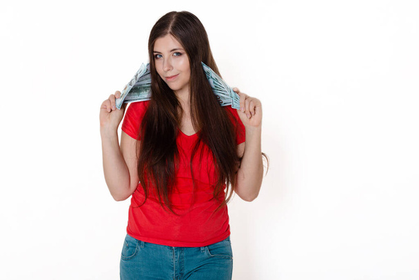 young, beautiful girl in a red t-shirt with money in hands. studio photo on a white background. - 写真・画像