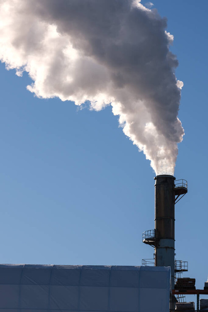 Une fumée épaisse s'écoule dans un ciel bleu, polluant l'air d'une grande cheminée de fumée. - Photo, image