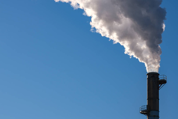 Thick smoke billows into a blue sky, polluting the air from a tall smokestack. - Photo, Image