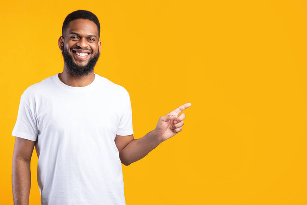 negro hombre señalando dedo aparte de pie sobre amarillo estudio fondo - Foto, Imagen