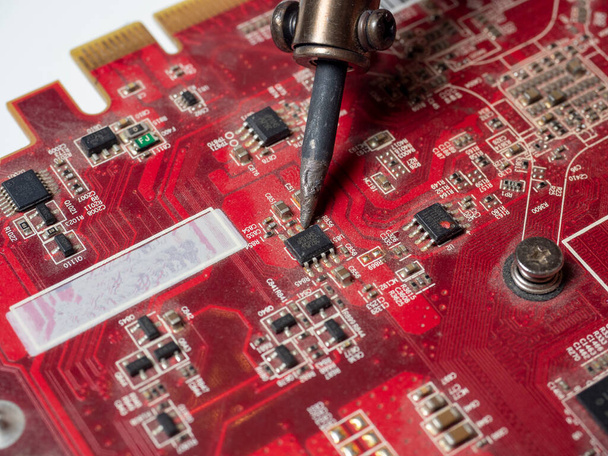 Un riparatore salda un circuito stampato di un dispositivo elettronico in primo piano di colore rosso. Riparazione e saldatura di trucioli con saldatore. Ingegnere tecnico in officina - Foto, immagini