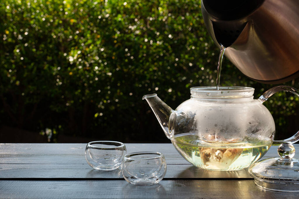 Bild von Menschen, die heißes Wasser in einen gläsernen Wasserkocher gießen, um nachmittags im Garten Tee zu kochen - Foto, Bild