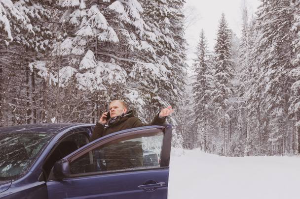 A young man in the winter on the car got lost and talking on the phone getting out of the car. Concept of winter road travel, road search, navigation.	 - Fotografie, Obrázek