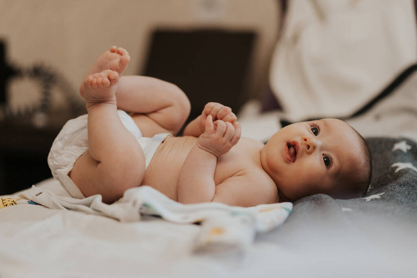 ベビーベッドの中に寝そべってカメラを見てきれいな柔らかい肌かわいい顔ベッドルームの新生児の幸せそうな顔。子供のテーマのための美しい背景 - 写真・画像