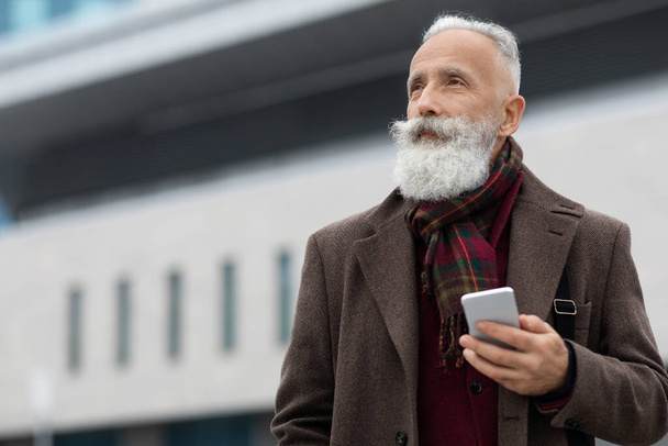 Senior grey-haired businessman using smartphone on the street, copy space - Fotoğraf, Görsel