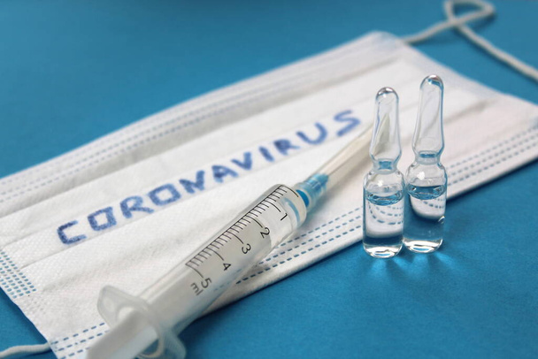 A face mask with the inscription coronavirus lies on a blue background with a syringe with a medicine for injection. - Foto, immagini