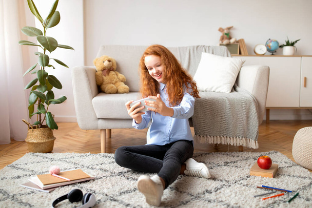 Dívka hraje hry na chytrý telefon odpočívá na podlaze - Fotografie, Obrázek