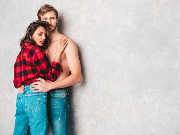 Hot beautiful woman and her handsome boyfriend. Models posing near gray wall in jeans clothes. Young passionate couple hugging before having sex. Sensual pair getting closer for kiss. Lover couple - Foto, Imagen