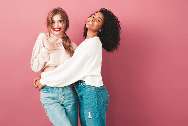 Two young beautiful smiling international hipster female in trendy summer jeans clothes. Sexy carefree women posing near pink wall in studio. Positive models having fun. Concept of friendship  - Фото, зображення