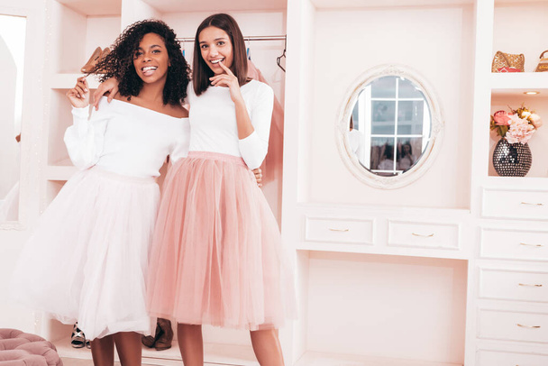 Two young beautiful smiling international hipster female in trendy summer dresses. Sexy carefree women posing in pink wardrobe. Positive models having fun. Concept of friendship  - Foto, imagen
