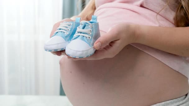 Primer plano de las pequeñas botas de bebé recién nacidas azules en las manos de yougn mujer embarazada - Metraje, vídeo