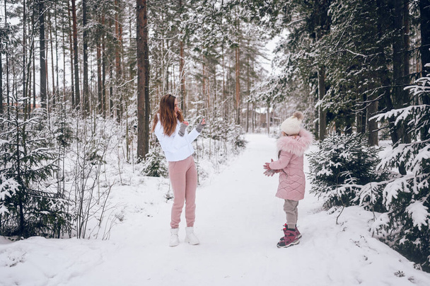 Szczęśliwa matka i mała słodka dziewczyna w różowej ciepłej bieliźnie spacery grając w walkę śnieżnej kuli zabawy w śniegu biały las iglasty zima ze świerkowym lesie na świeżym powietrzu. Rodzinne zajęcia sportowe - Zdjęcie, obraz
