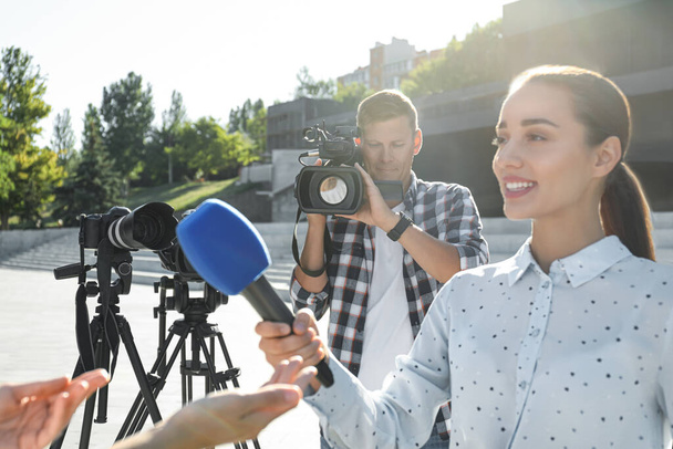 Professional journalist and operator with video camera taking interview outdoors - Zdjęcie, obraz