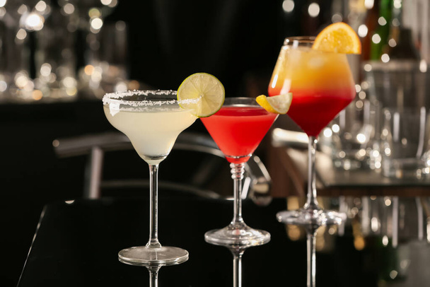 Different delicious cocktails on black table in bar - Фото, изображение