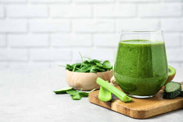Delicious green juice and fresh ingredients on table against brick wall, space for text - 写真・画像
