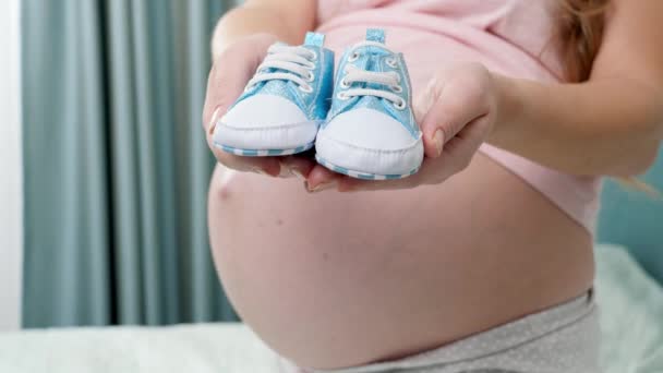 Close-up van mooie zwangere vrouw met grote buik wachten voor baby jongen met kleine laarzen op handen - Video