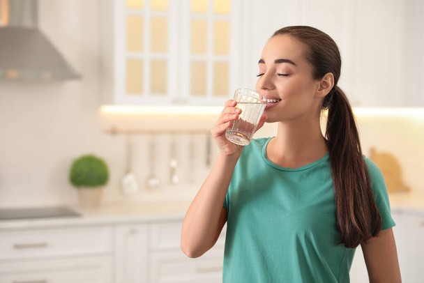 Young woman drinking pure water from glass in kitchen. Space for text - Photo, image