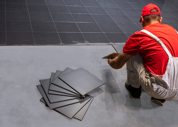 Ein Bauarbeiter legt neue Bodenfliesen an. - Foto, Bild