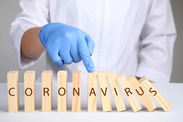Doctor stopping domino effect at white table, closeup. Prevent spreading of coronavirus - Valokuva, kuva