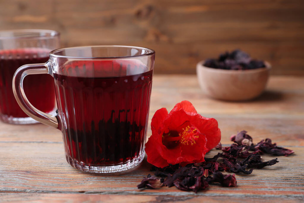 Delicious hibiscus tea and dry flowers on wooden table - Foto, Bild