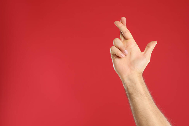 Man with crossed fingers and space for text on red background, closeup. Superstition concept - Photo, Image