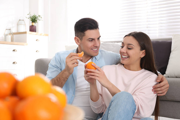 Happy couple with tangerines near sofa at home - Φωτογραφία, εικόνα