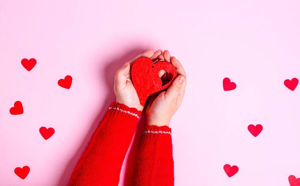 Child's hands hold a wooden red heart on a pink background. Love concept, copy space, flat lay, place for text, banner, top view. - Fotografie, Obrázek