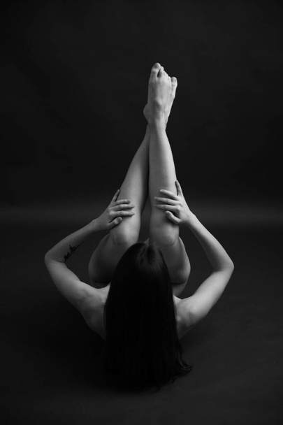 Black and white photo of body parts. Geometry and yoga poses of a naked female body on a dark background. Space for text - Zdjęcie, obraz