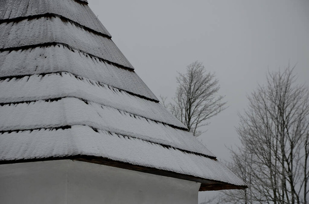 techo de madera de tejas en un edificio en las montañas. nieve y hielo cubierto de tejas astilladas. marrón, negro y blanco son muy variados texturalmente y no parecen monótonos. - Foto, Imagen