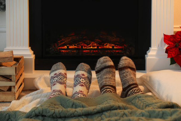 Couple in warm socks resting near fireplace at home, closeup - Foto, Bild