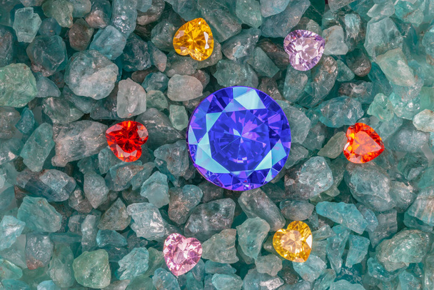 Μπλε Ζαφείρι διαμάντια τοποθετούνται σε ένα θύλακα από πολύχρωμα διαμάντια σε σχήμα καρδιάς σε ακατέργαστο ουρανό μπλε πολύτιμους λίθους - Φωτογραφία, εικόνα